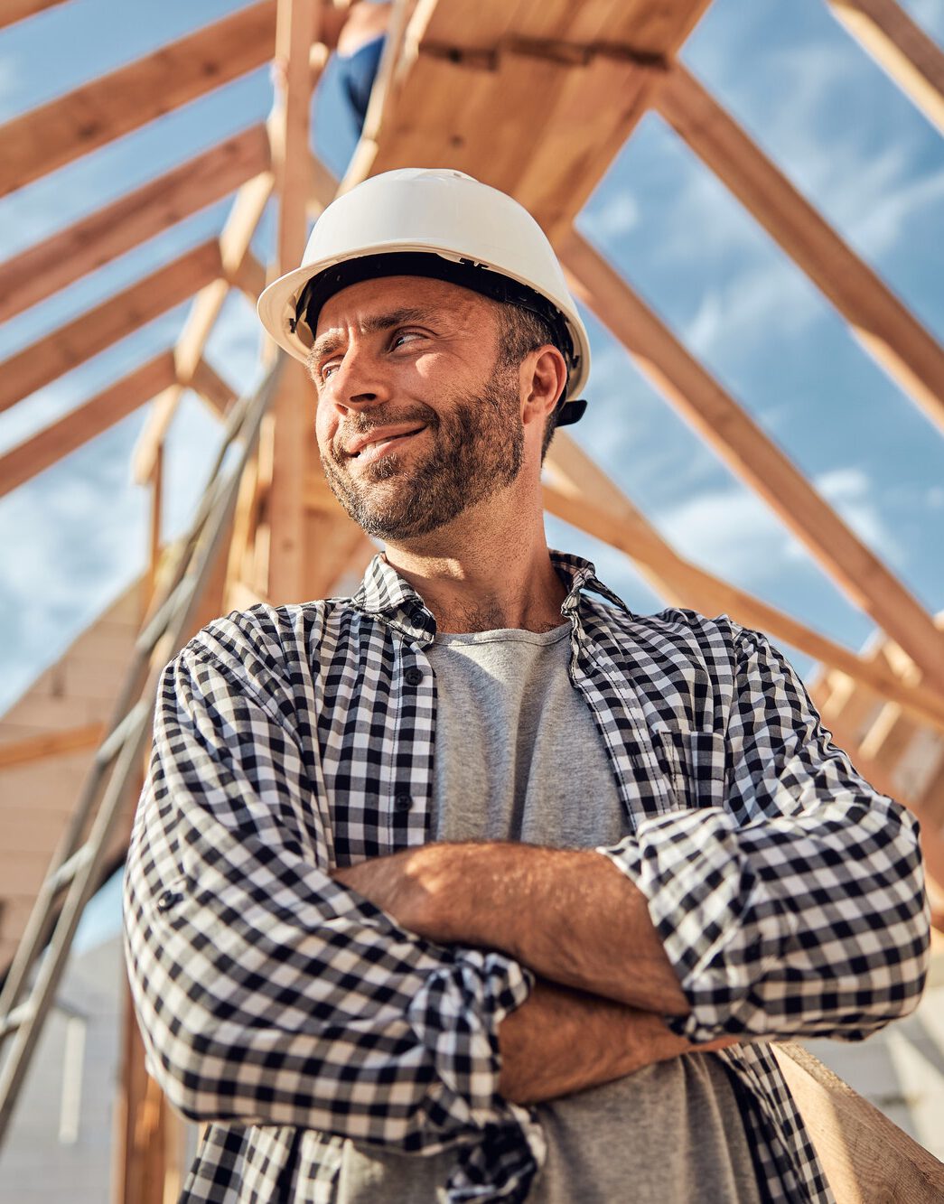 Pleased man in a hard hat posing under a wooden roof